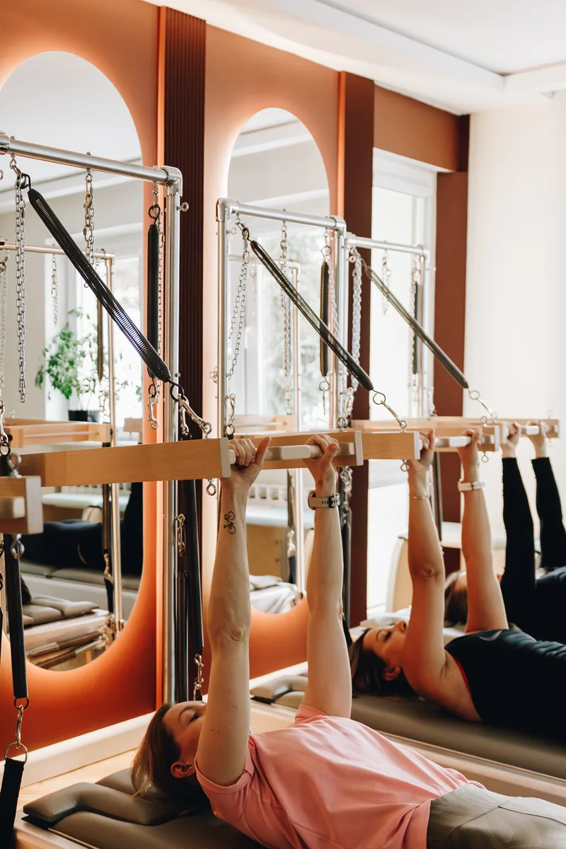 Grupowy trening Pilates na reformerach w nowoczesnym studio z pomarańczowymi elementami.