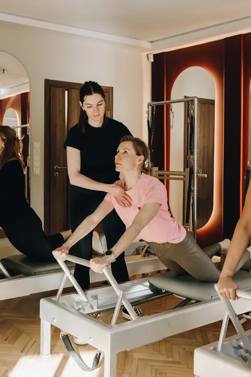 Kobieta ćwiczy na reformerze do pilatesu pod okiem nauczycielki.