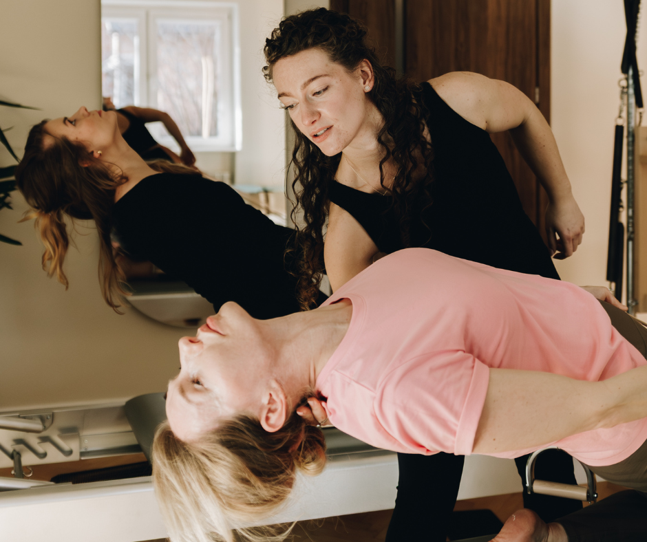 Nauczycielka pilates asekuruje kobietę podczas wygięcia w tył na reformerze do pilatesu.