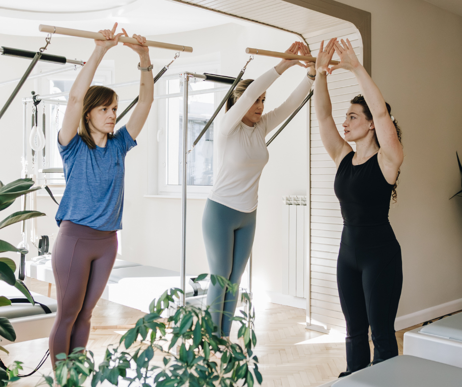 Trzy kobiety ćwiczą Pilates na maszynie Cadillac w jasnym studiu pod okiem instruktorki.